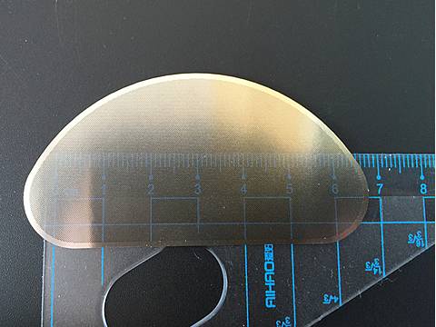 A piece of arched etched plates are put under a ruler to show dimension.