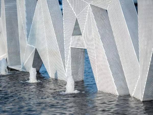 Building decorated with white perforated metal sheets over water