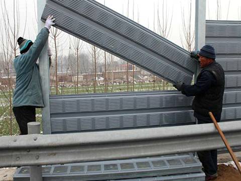 Two workers are installing the noise barrier panel into the space between posts.