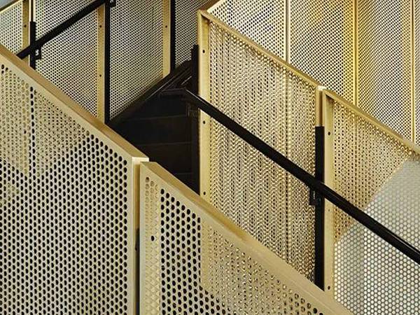 Handrails on both sides of stairs made of perforated brass sheets with round holes