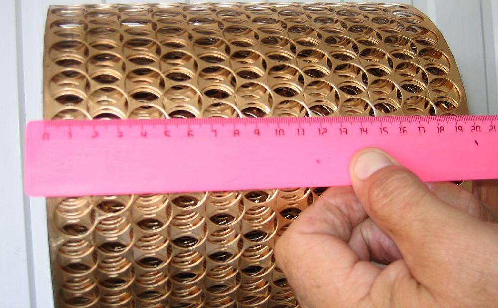 A man is measuring the width of a roll of perforated copper belt