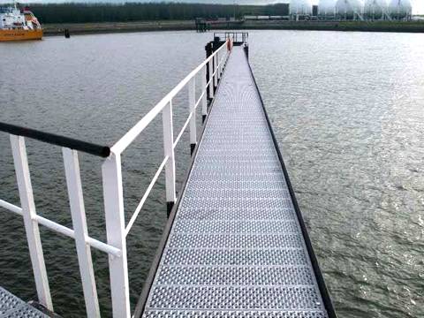 Perforated-o safety grating planks are built into a riverside sidewalk with rails.