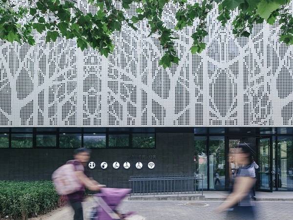 2 men pass in front of a white perforated sheet decorated building facade